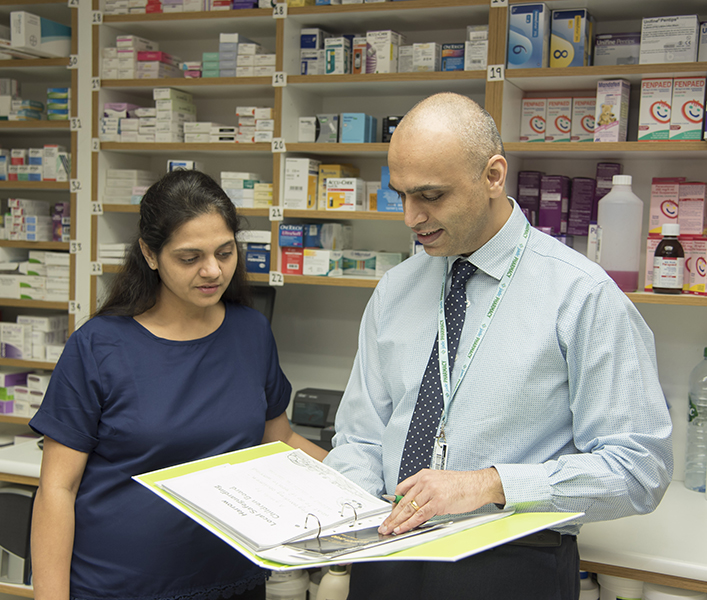 two people in community pharmacy looking at a binder