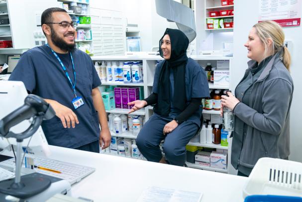 Three pharmacy professionals having a conversation behind a pharmacy counter